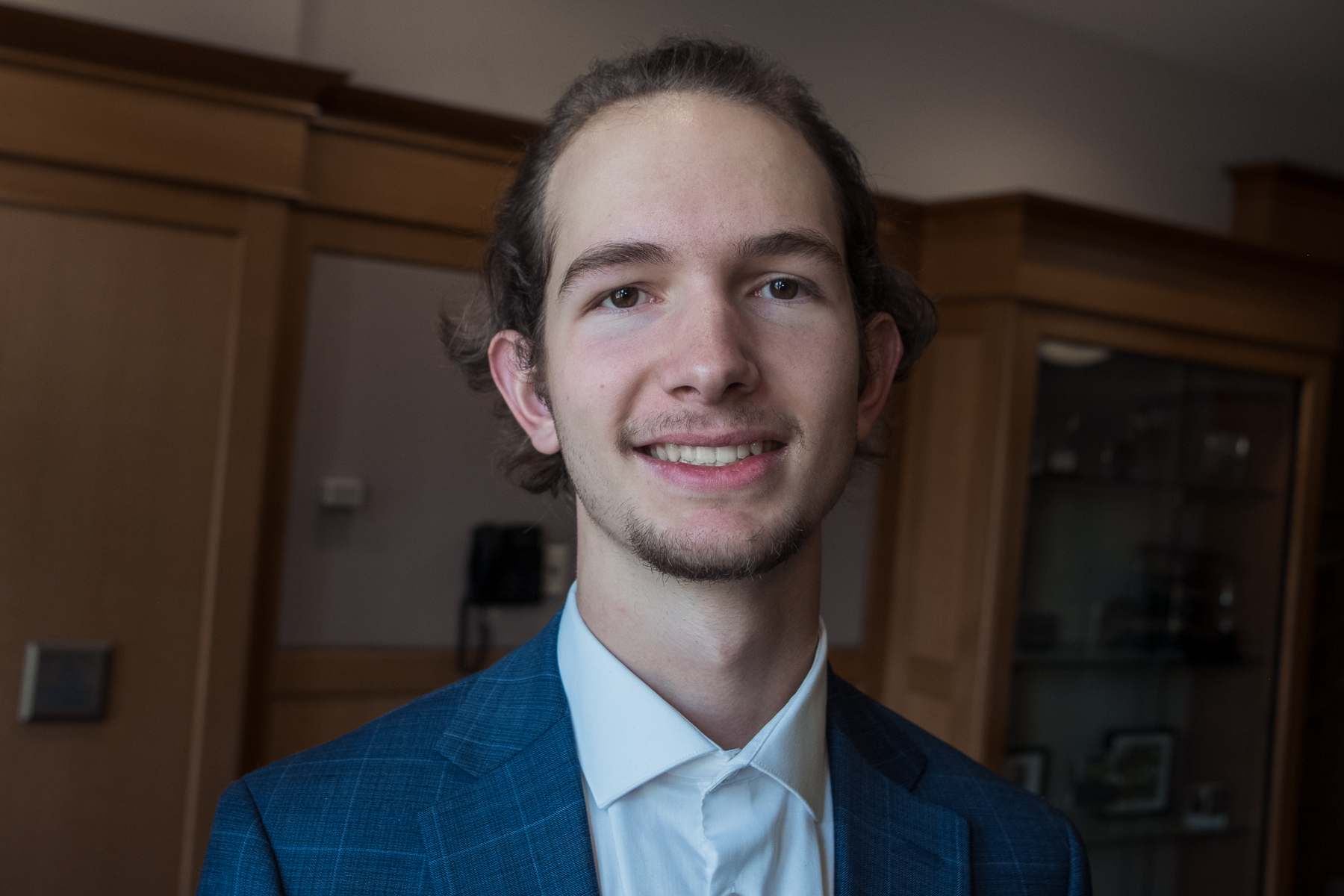 Professional headshot of a young man in a blue suit smiling warmly